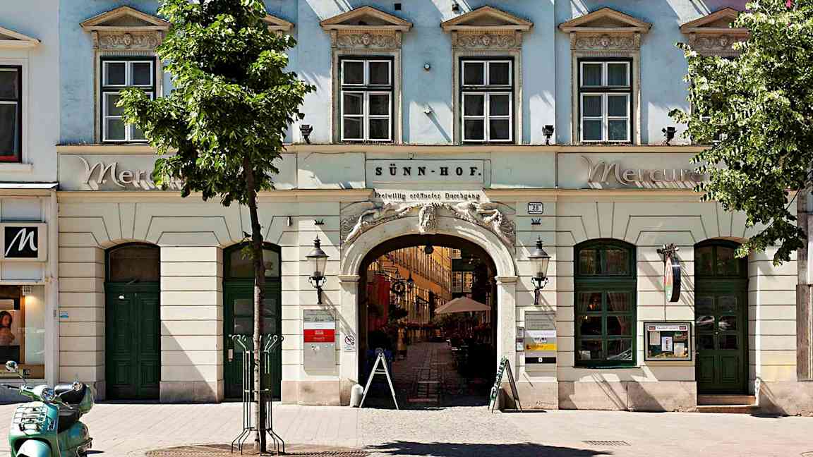 Rakennus, jossa on ikkunoita, kaariportti ja kukkalaatikot ikkunoiden vieressä. (Tekoälyn luoma teksti)