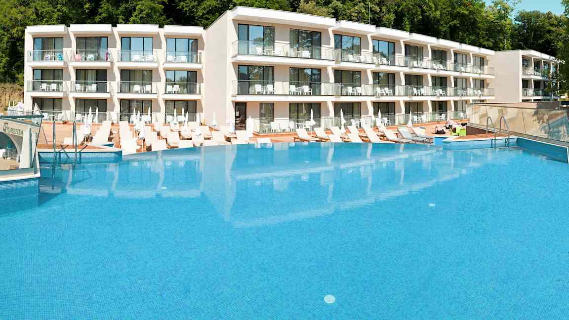 Hotellikompleksi, jonka edessä suuri uima-allas ja ympärillä aurinkotuoleja. (Tekoälyn luoma teksti)