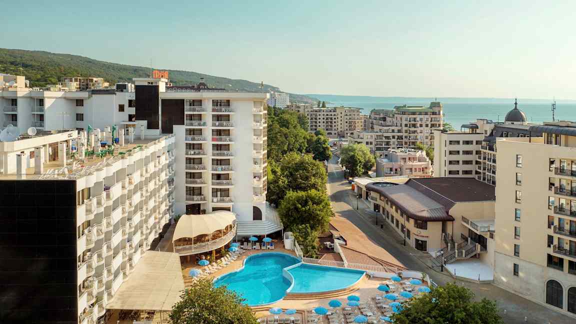 Hotellirakennukset ulkouima-altaalla ja aurinkotuoleilla, ympärillä muita rakennuksia lähellä merta. (Tekoälyn luoma teksti)