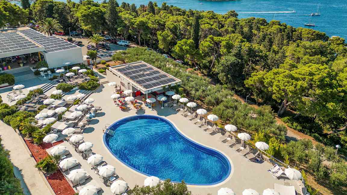 Näkymä ulkouima-altaasta, jota ympäröivät aurinkotuolit ja aurinkovarjot, sijaitsee lähellä rannikkoa metsän ja meren äärellä. (Tekoälyn luoma teksti)