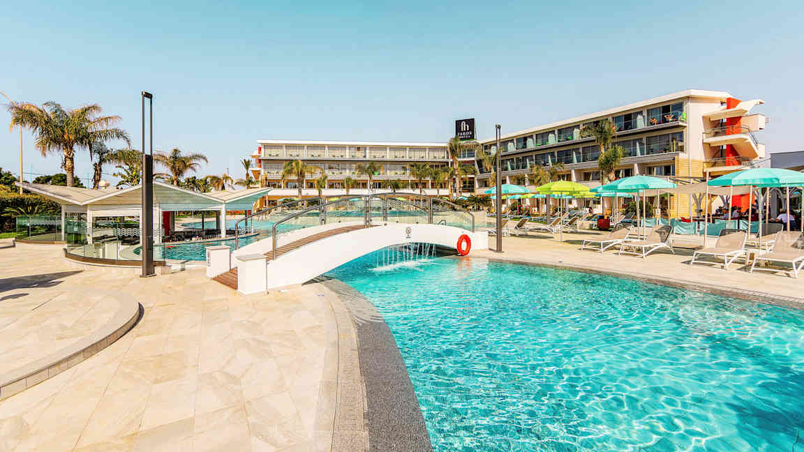 Kuva uima-altaasta, jossa on pieni silta ja hotellirakennus taustalla. (Tekoälyn luoma teksti)