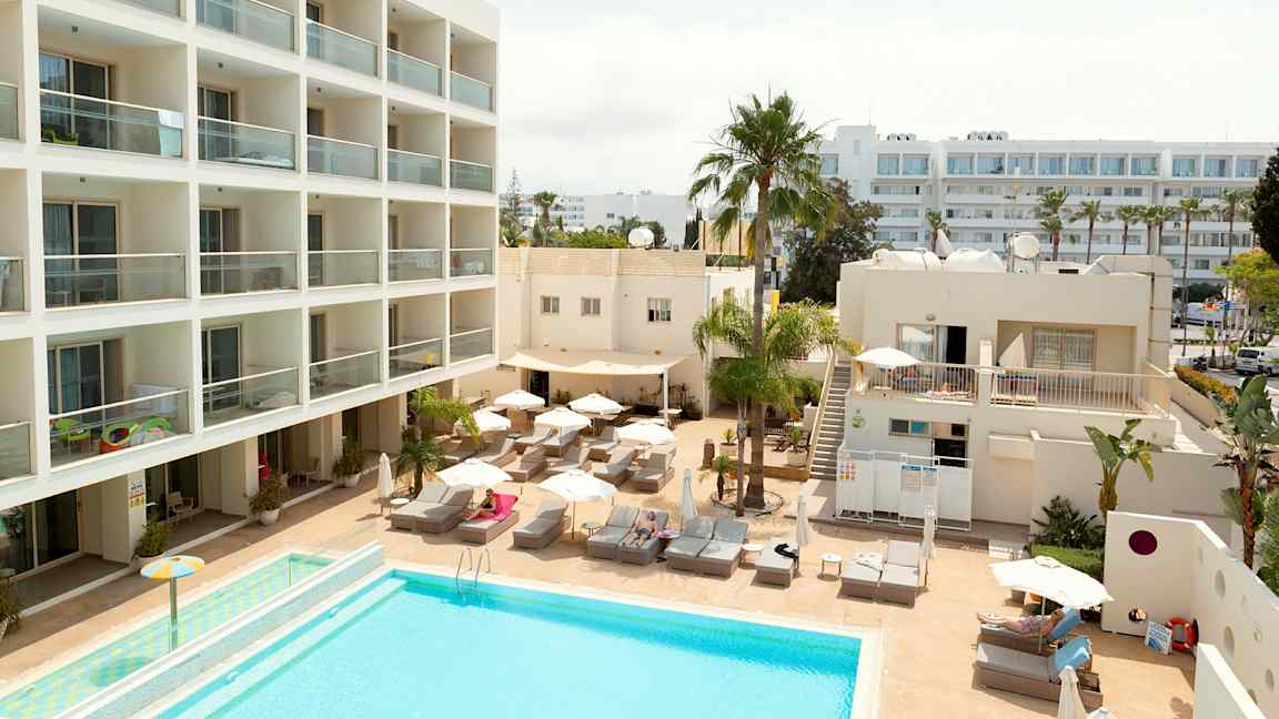 Hotellialue, jossa uima-allas, aurinkotuoleja ja rakennuksia. (Tekoälyn luoma teksti)