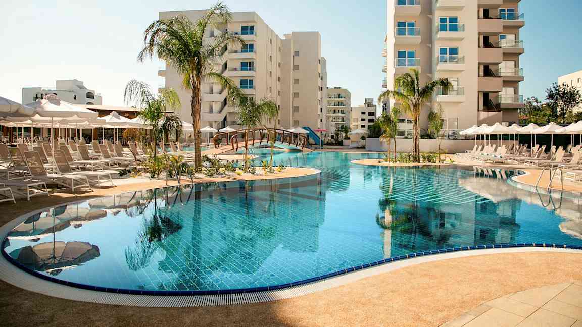 Ulkouima-allas, jota ympäröivät aurinkotuolit ja aurinkovarjot, taustalla korkeat rakennukset. (Tekoälyn luoma teksti)