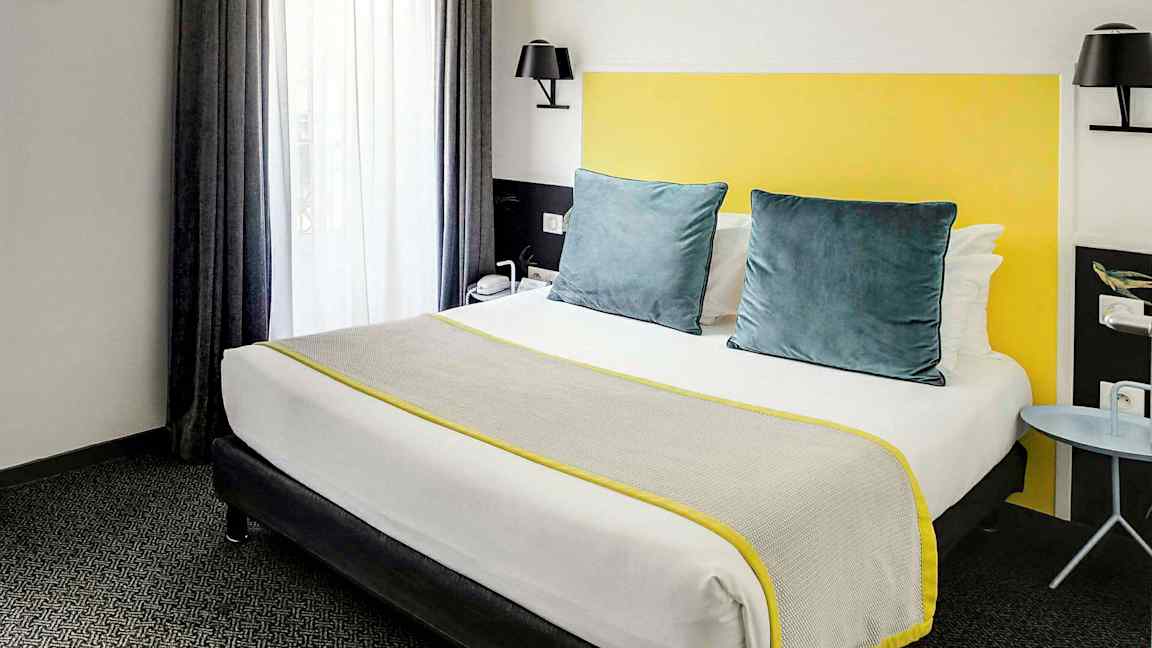 Hotellihuone, jossa on harmailla ja keltaisilla yksityiskohdilla varustettu sänky. (Tekoälyn luoma teksti)