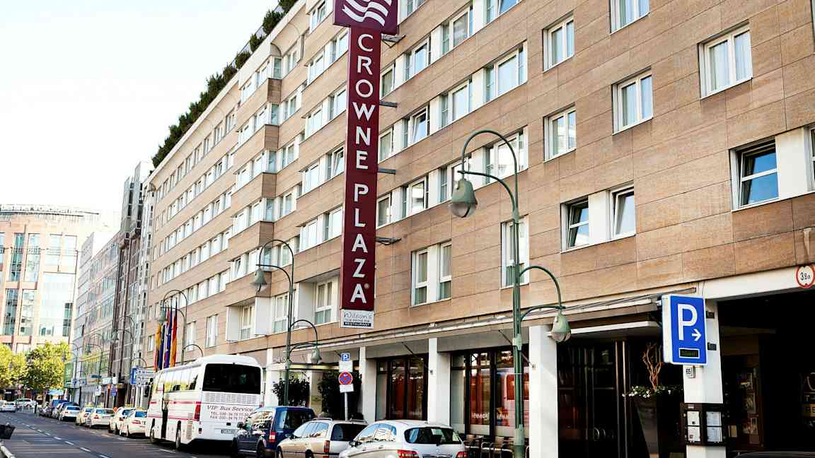 Crowne Plaza -hotellirakennus, jossa pysäköintimerkki ja bussi edessä. (Tekoälyn luoma teksti)
