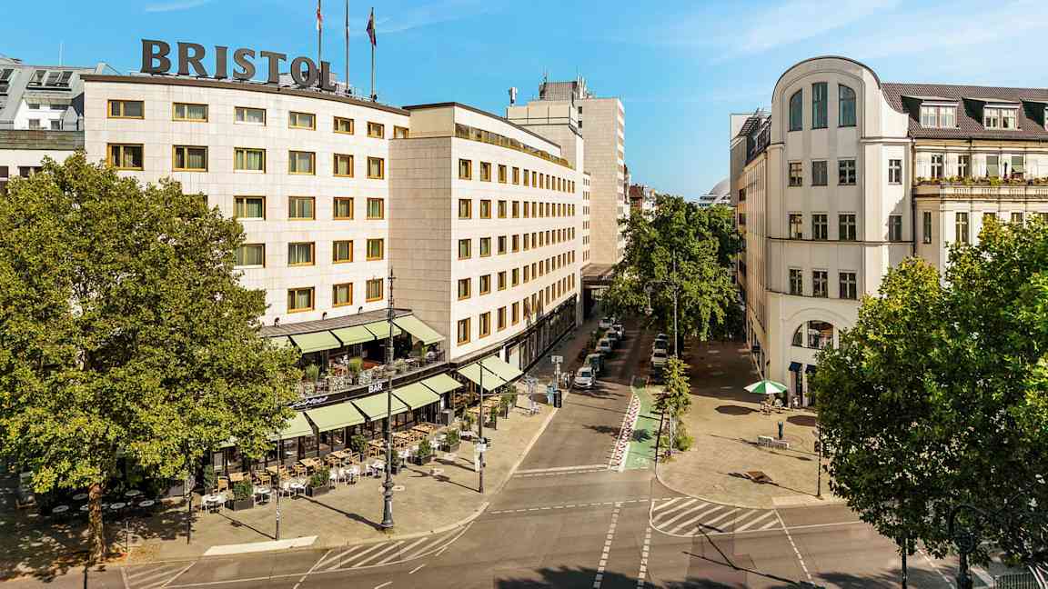 Kaupunkimaisema, jossa on rakennus, jonka katolla lukee "Bristol", ympärillä puita ja katu ulkoilmaravintoloineen. (Tekoälyn luoma teksti)