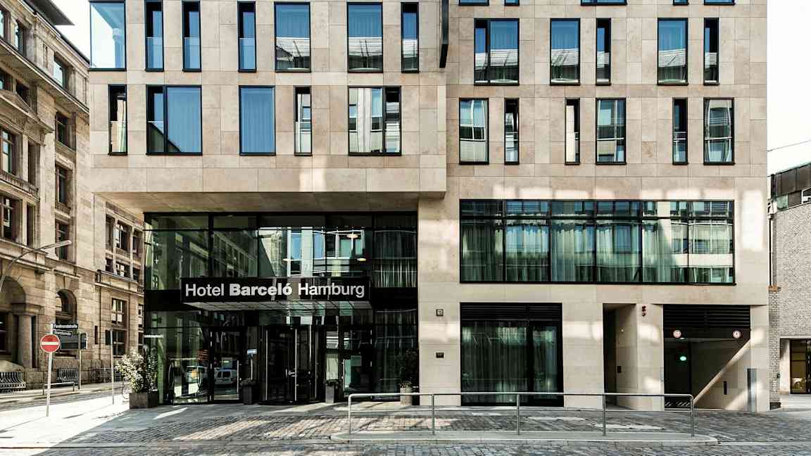 Rakennus, jossa on moderni julkisivu ja sisäänkäynti, jonka yläpuolella lukee "Hotel Barceló Hamburg". (Tekoälyn luoma teksti)