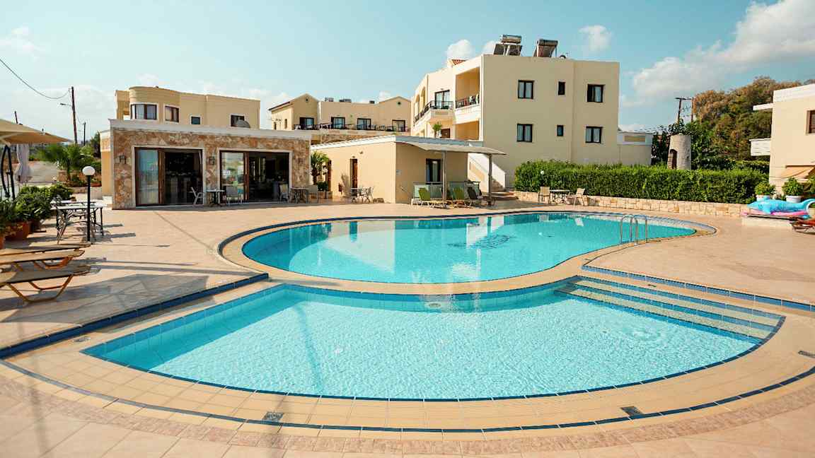 Kuva, jossa näkyy ulkouima-allas, jota ympäröivät aurinkotuolit ja taustalla on rakennuksia. (Tekoälyn luoma teksti)