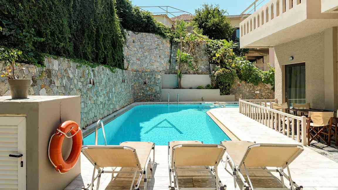 Uima-allas, jota ympäröi kivimuuri ja vehreys. Aurinkotuoleja on altaan reunalla. (Tekoälyn luoma teksti)