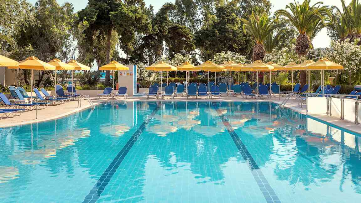 Ulkouima-allas, jossa sinistä vettä, ympäröitynä aurinkotuoleilla, aurinkovarjoilla ja vihreillä puilla. (Tekoälyn luoma teksti)