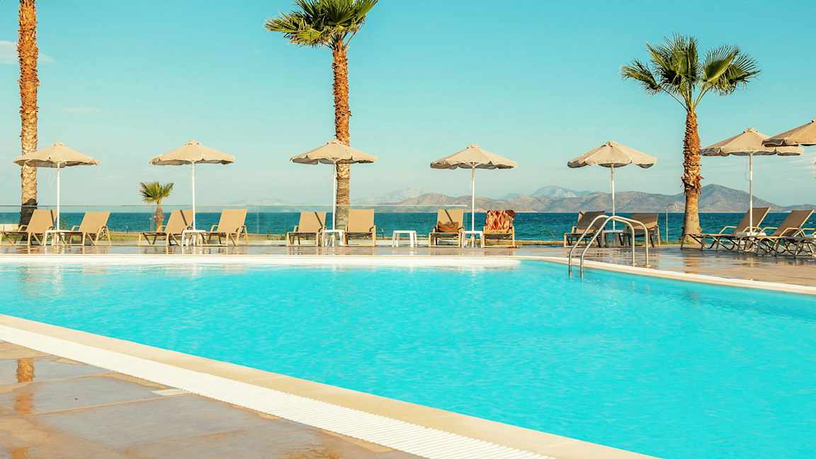 Uima-allas aurinkotuoleilla ja varjoilla, taustalla meri ja vuoret. (Tekoälyn luoma teksti)