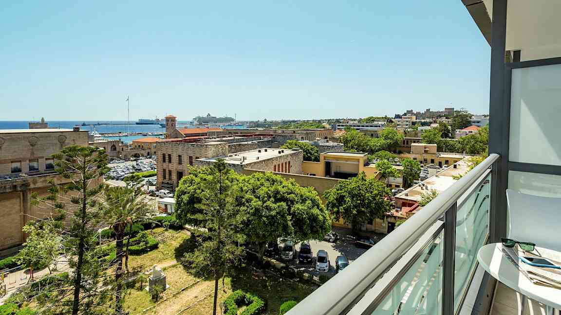 Näköala parvekkeelta kaupungille, jossa on historiallisia rakennuksia, puita ja satama veneineen. (Tekoälyn luoma teksti)