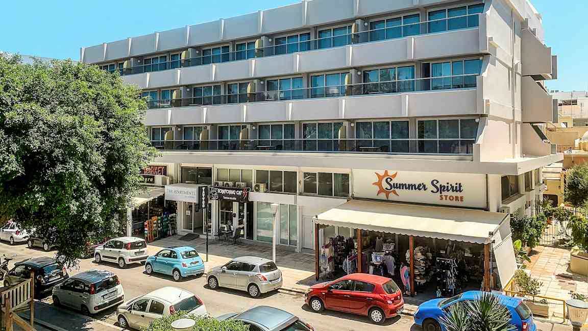 Moderni rakennus, jossa on useita kerroksia ja kauppoja pohjakerroksessa. Rakennuksen edessä on pysäköityjä autoja. (Tekoälyn luoma teksti)