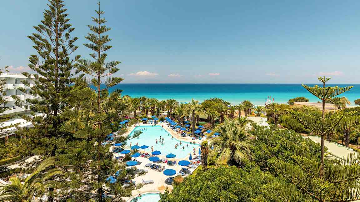 Kuva hotellialueesta, jossa uima-allas ja aurinkotuolit, ympärillä vehreyttä ja näkymä merelle. (Tekoälyn luoma teksti)