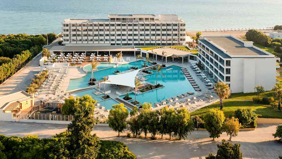 Ilmakuva hotellikompleksista, jossa on uima-allasalue ja meri taustalla. (Tekoälyn luoma teksti)