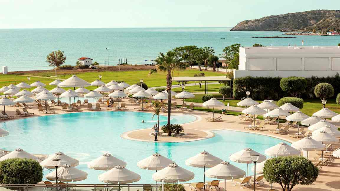 Uima-allas, jossa aurinkotuoleja ja varjoja, näkymät merelle ja vehreään ympäristöön. (Tekoälyn luoma teksti)