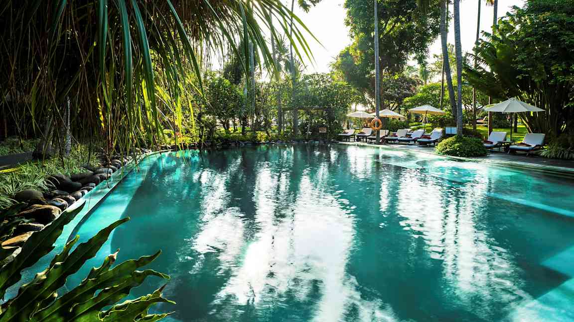 Ulkouima-allas, jota ympäröivät trooppiset kasvit ja palmut auringonlaskun aikaan. (Tekoälyn luoma teksti)