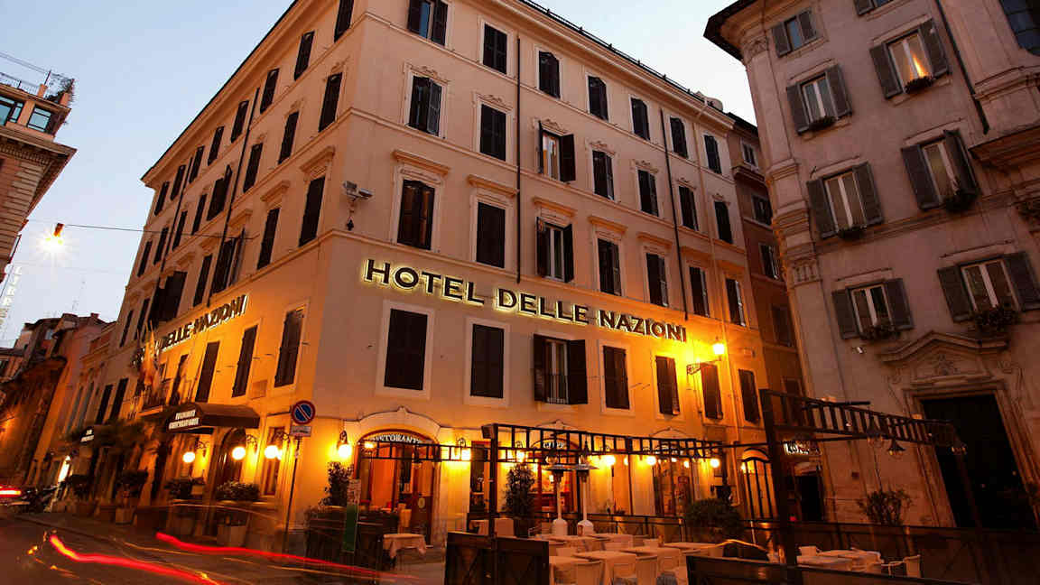 Kuva rakennuksesta, jossa kyltti, joka sanoo Hotel Delle Nazioni, valaistu iltavalaistuksella. (Tekoälyn luoma teksti)