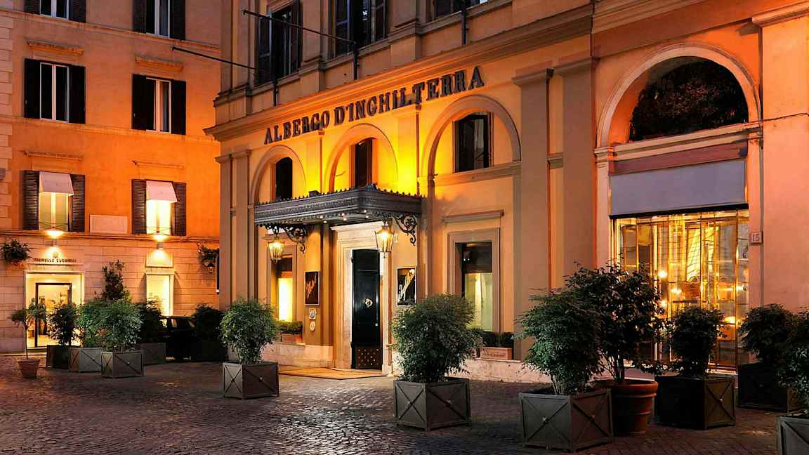 Hotelli, jonka sisäänkäyntiä koristaa kaarihallikäytävä ja jossa on valoja illalla. (Tekoälyn luoma teksti)