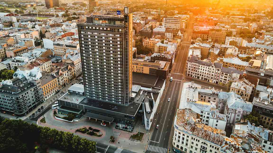Ilmakuva kaupungista, jonka etualalla on korkea rakennus ja ympärillä muita rakennuksia, auringon laskiessa horisontissa. (Tekoälyn luoma teksti)