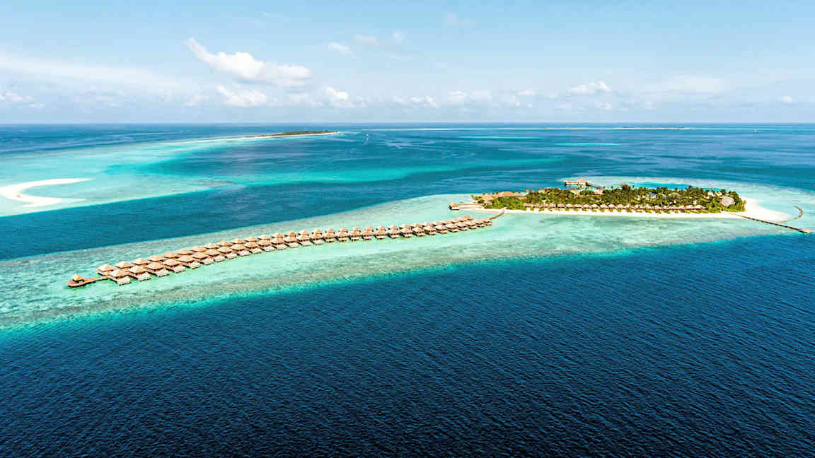 Ilmakuva trooppisesta saaresta ja veden ylle rakennetuista huviloista kirkkaansinisessä meressä. (Tekoälyn luoma teksti)