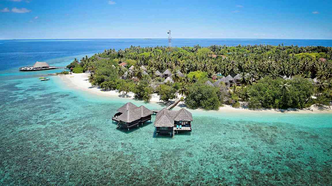 Trooppinen saari, jolla on puisia bungaloweja veden yläpuolella ja sitä ympäröivät vihreät kasvillisuudet. (Tekoälyn luoma teksti)