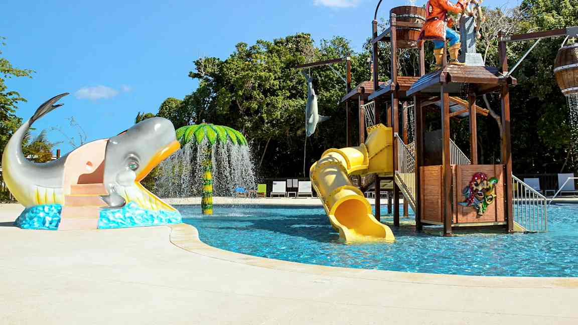 Lasten uima-allas, jossa vesiliukumäkiä, merirosvoteema ja hahmoja, kuten valas ja palmu. (Tekoälyn luoma teksti)