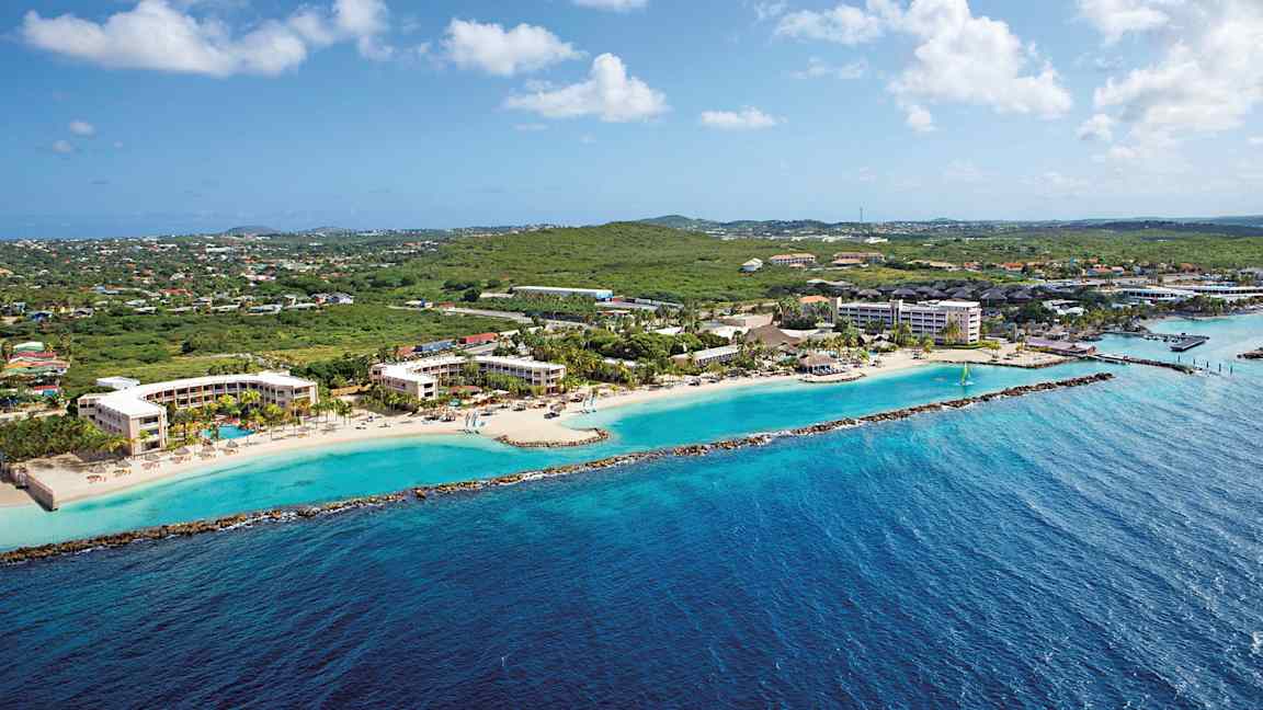 Ilmakuva rannikosta, jolla on hotellirakennuksia rannalla ja vehreyttä taustalla. (Tekoälyn luoma teksti)