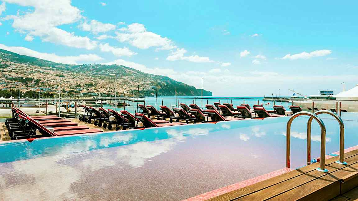 Infinity-allas, josta näkymä aurinkotuoleille, merelle ja ympäröivään vuoristoon. (Tekoälyn luoma teksti)