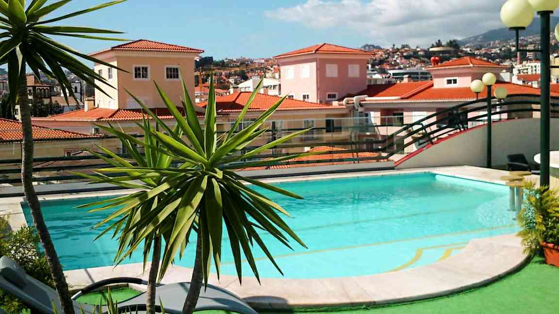 Uima-allas, jota ympäröi vehreys, ja taustalla on punatiilikattoisia taloja. (Tekoälyn luoma teksti)