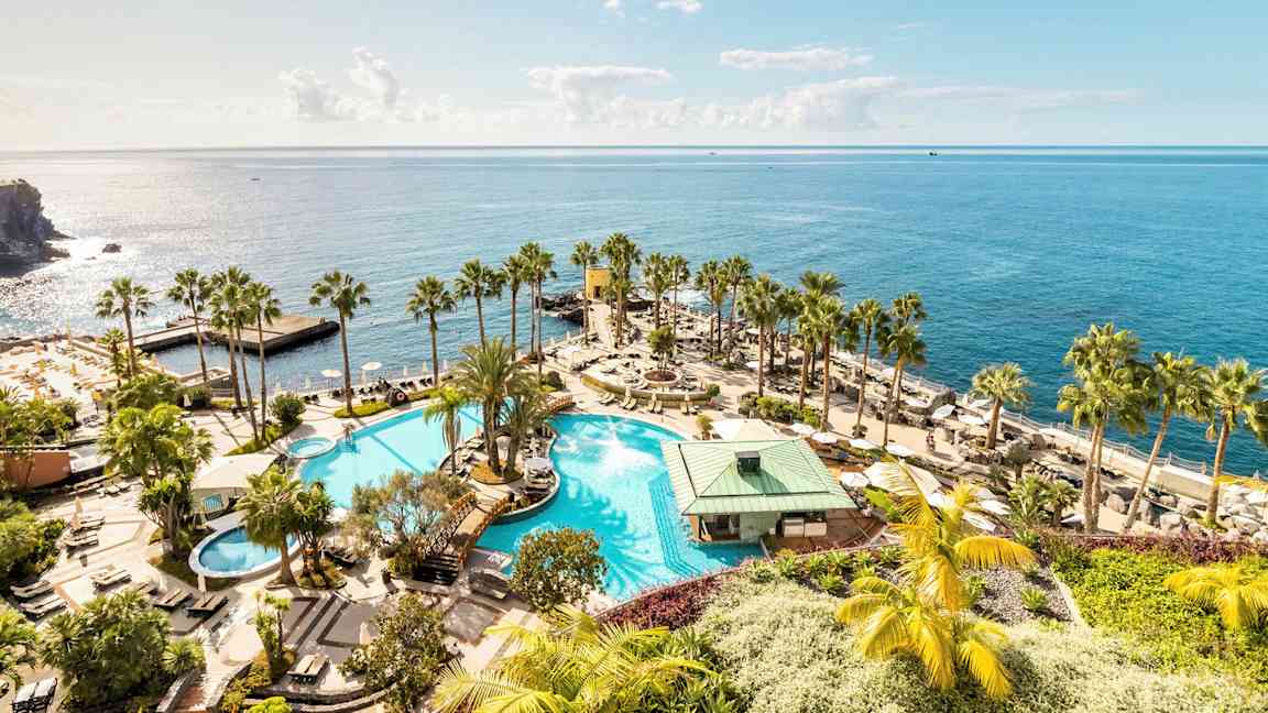 Suuri uima-allas ympäröitynä palmuilla ja aurinkotuoleilla, sijaiten rannan läheisyydessä ja avautuu kimaltelevalle merelle. (Tekoälyn luoma teksti)