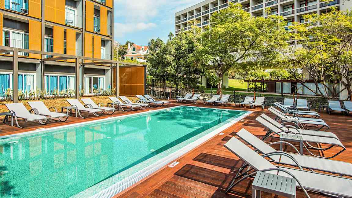 Uima-allas, jossa aurinkotuoleja ja taustalla rakennuksia. (Tekoälyn luoma teksti)