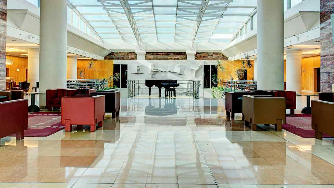 Valoisa ja tilava hotellin aula, jossa istuinryhmiä ja piano. (Tekoälyn luoma teksti)