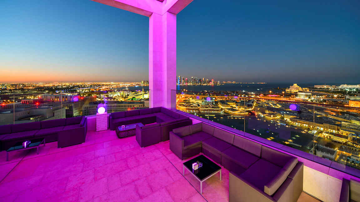 Terassi, jossa on istumapaikkoja ja näkymä kaupunkiin iltahämärässä. (Tekoälyn luoma teksti)