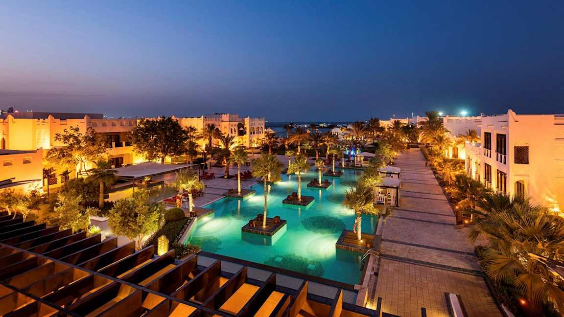 Valaistu lomakohde, jossa on uima-altaita ja palmuja illalla. (Tekoälyn luoma teksti)