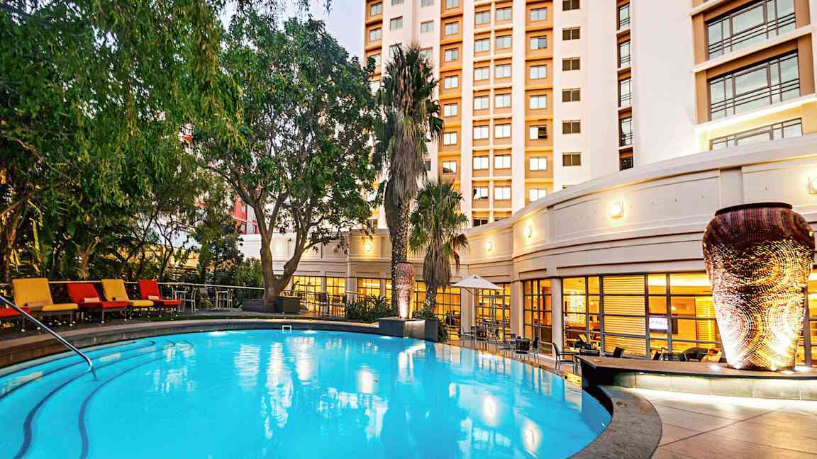 Valaistu ulkouima-allas, jota ympäröivät vihreät kasvit ja taustalla oleva rakennus. (Tekoälyn luoma teksti)