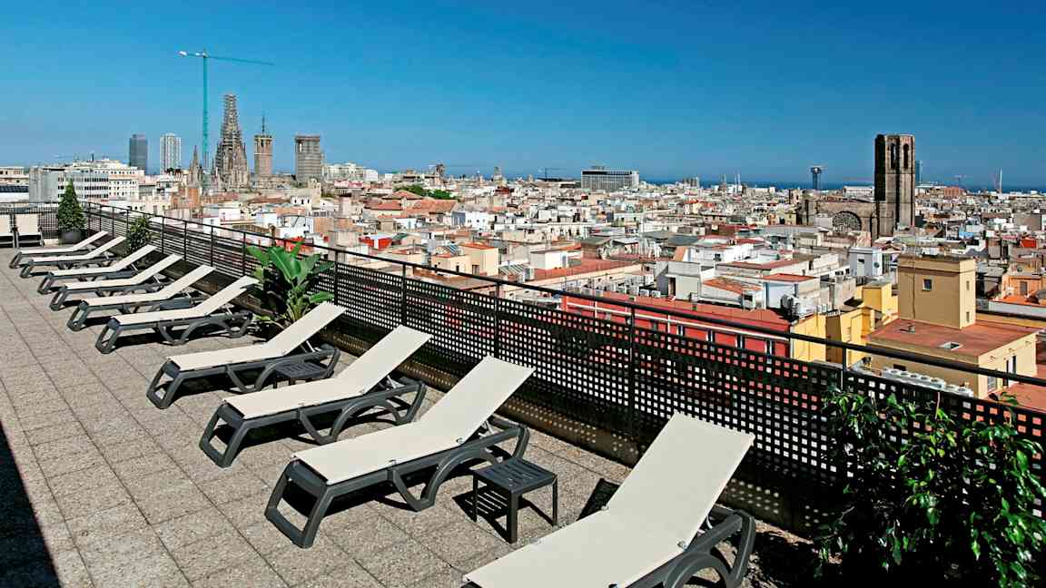 Kattoterassi aurinkotuoleilla ja näkymä kaupunkiin, jossa on kirkko ja sininen taivas. (Tekoälyn luoma teksti)