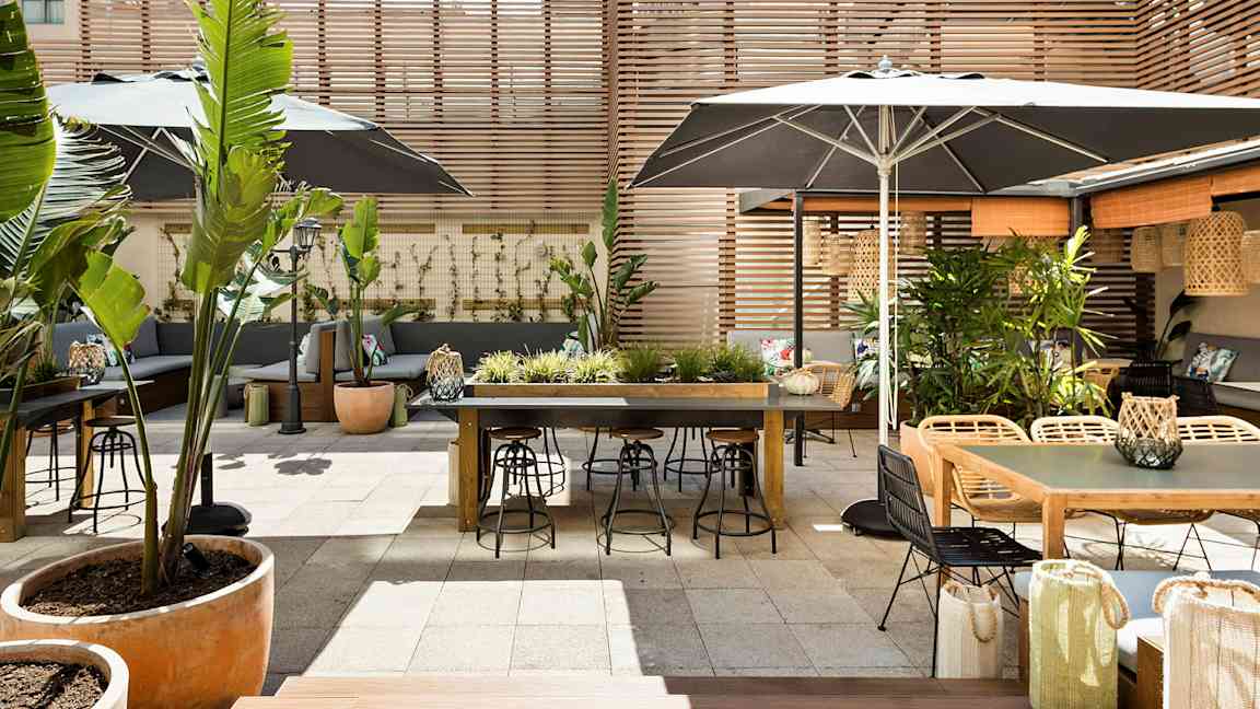 Ulkoterassi, jossa on pöytiä, tuoleja ja kasviasetelmia, puupaneeleilla ympäröity. (Tekoälyn luoma teksti)