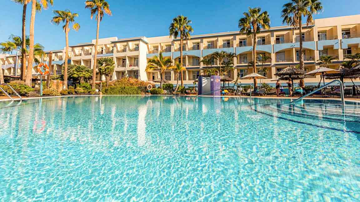 Ulkoallas, jota ympäröivät palmut ja taustalla hotelli. (Tekoälyn luoma teksti)