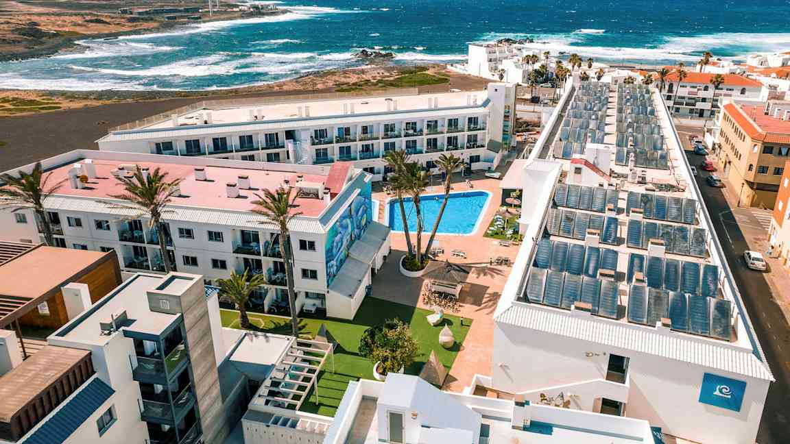 Hotellialue, jossa on uima-allas, rakennusten ympäröimänä, näkymä merelle ja aaltoihin. (Tekoälyn luoma teksti)