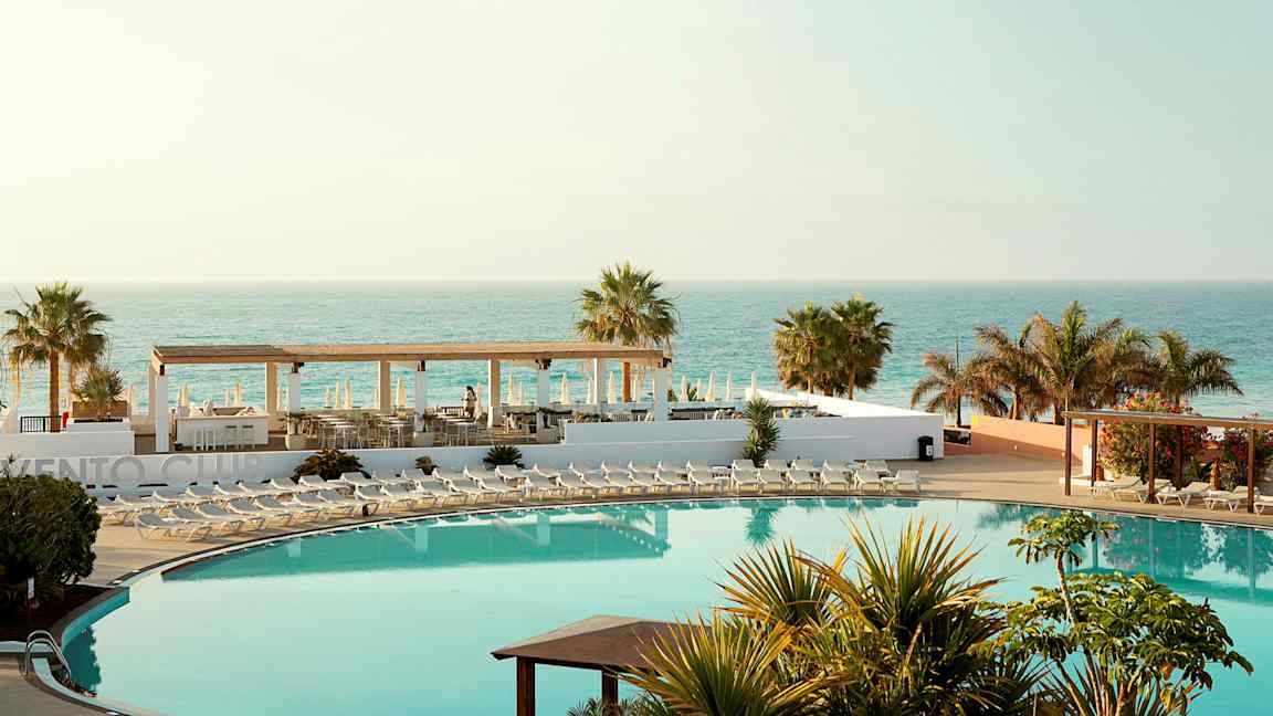 Hotellialue, jossa uima-allas, aurinkotuoleja, palmuja ja merinäköala. (Tekoälyn luoma teksti)