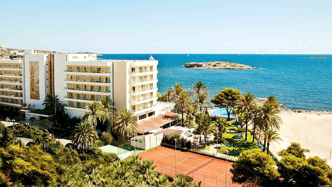 Kuva lomakeskuksesta rannalla, jossa rakennus, palmuja, uima-allas ja tenniskentät meren äärellä. (Tekoälyn luoma teksti)