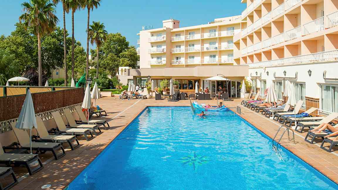 Hotellirakennus näkyy ulkouima-altaan vieressä, ympärillä aurinkotuoleja ja aurinkovarjoja. (Tekoälyn luoma teksti)