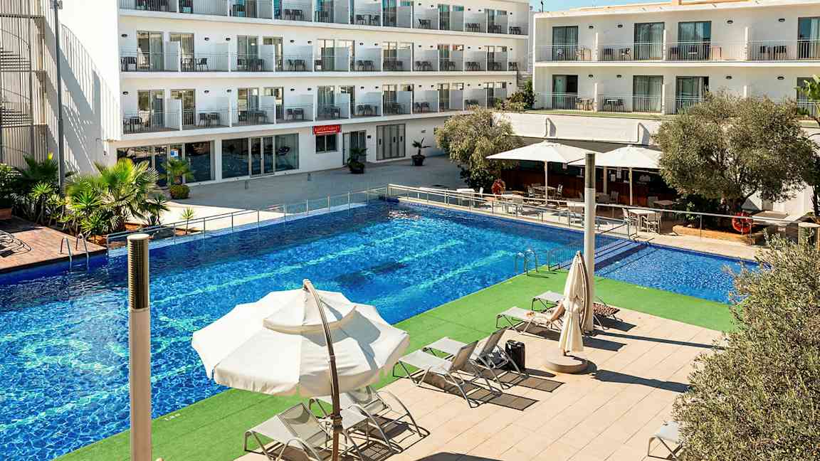 Kuva hotellirakennuksesta, jossa on useita kerroksia. Rakennuksen edessä on suuri uima-allas ja aurinkotuoleja varjojen alla. (Tekoälyn luoma teksti)