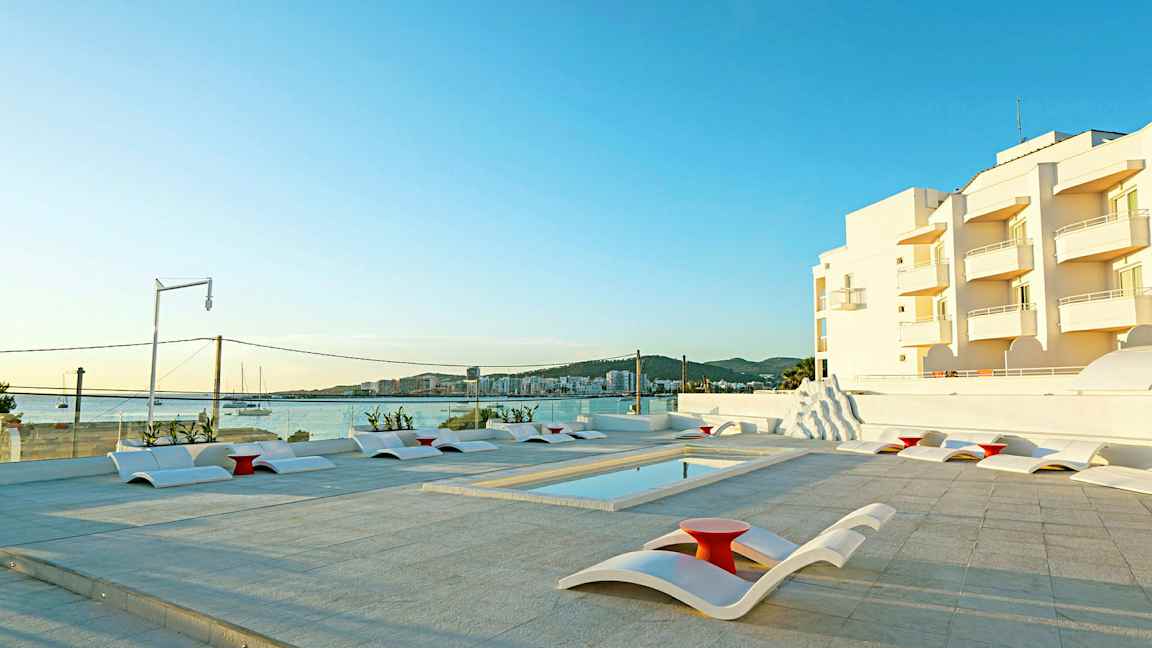 Ulkoaltaan alue nykyaikaisilla aurinkotuoleilla, näkymä merelle ja valkoisia rakennuksia taustalla. (Tekoälyn luoma teksti)