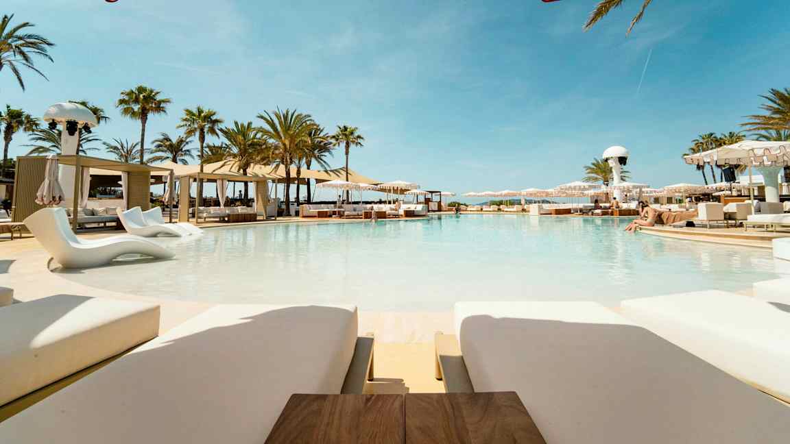 Ylellinen uima-allas, jota ympäröivät aurinkotuolit ja aurinkovarjot kesäisessä ympäristössä. (Tekoälyn luoma teksti)