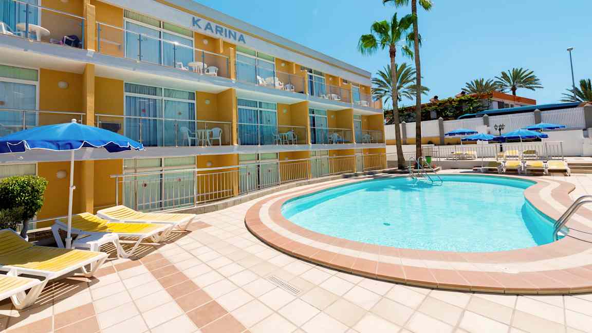 Ulkoallas, jonka ympärillä aurinkotuoleja, lähellä kerrostaloa ja palmuja. (Tekoälyn luoma teksti)