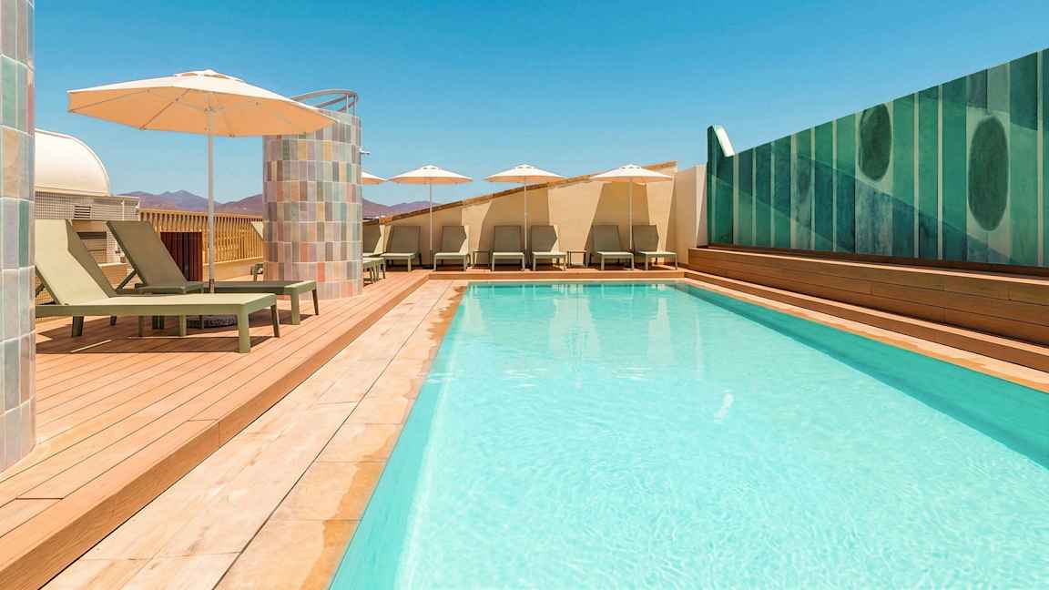Ulkouima-allas, jossa kirkas sininen vesi, ympärillä aurinkotuoleja ja varjoja puukannen päällä. (Tekoälyn luoma teksti)