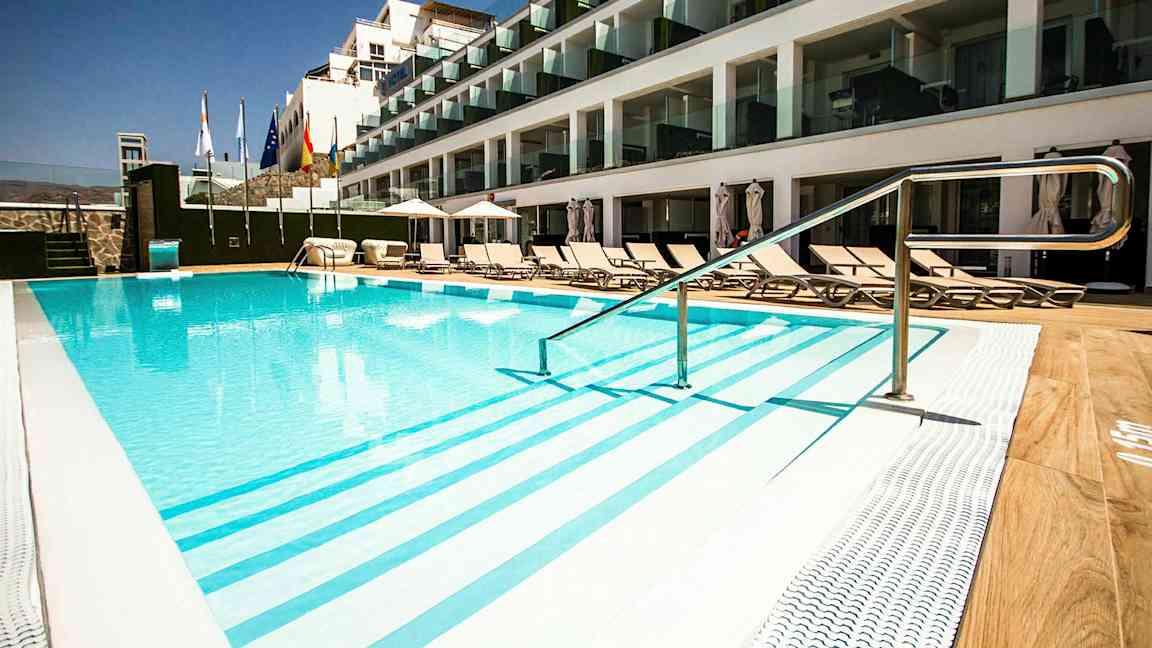 Ulkouima-allas hotellilla, jossa on aurinkotuoleja ja lasiparvekkeita. (Tekoälyn luoma teksti)