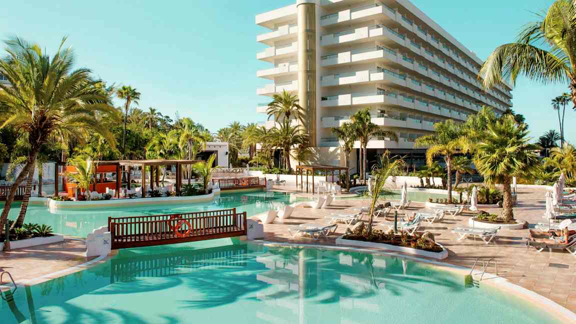 Hotelli, jossa on uima-allasalue, aurinkotuoleja ja palmuja. (Tekoälyn luoma teksti)